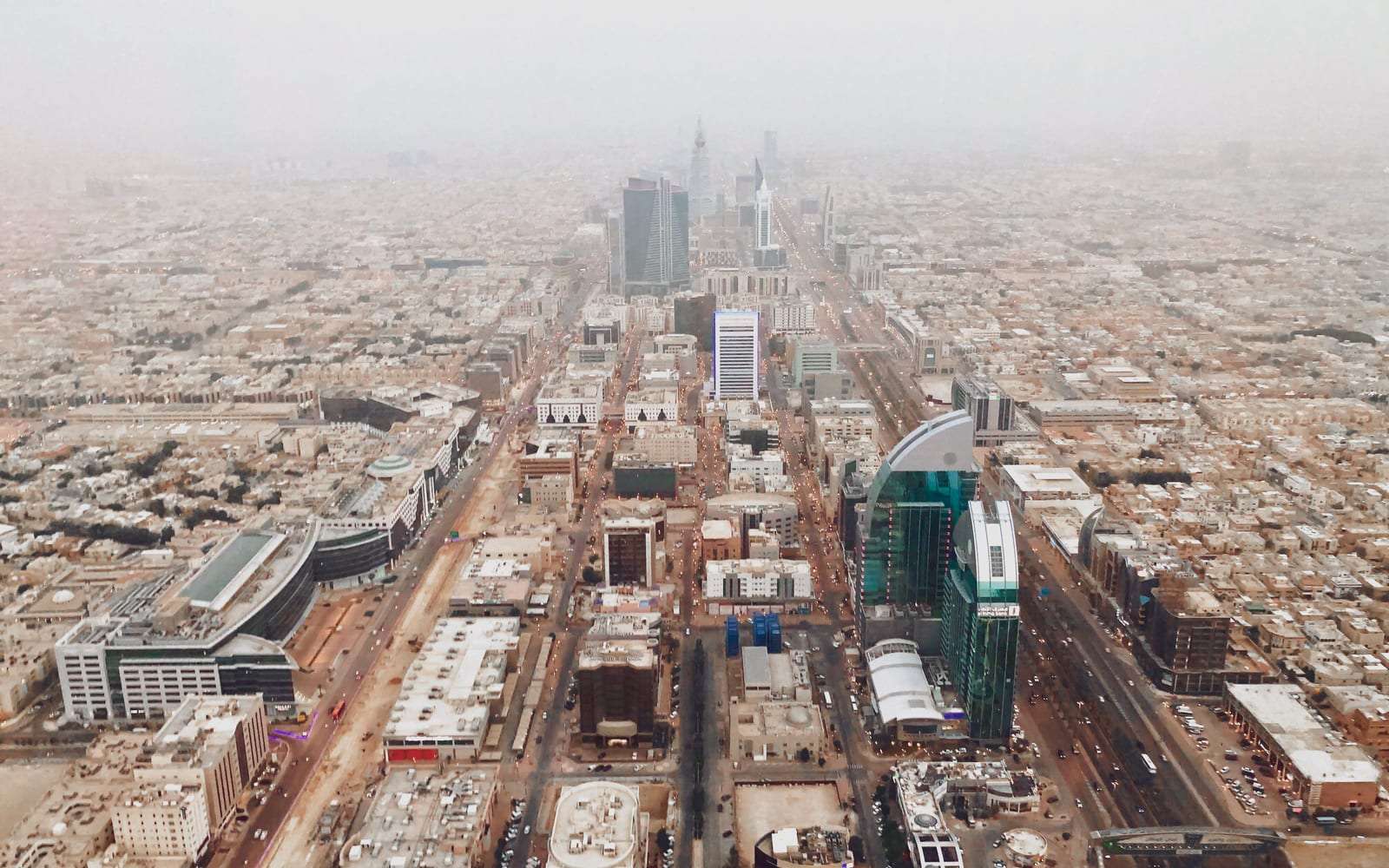 منظر جوي لشارع رئيسي في الرياض تمتد على جانبيه المباني تحت أفق مغبر قليلاً